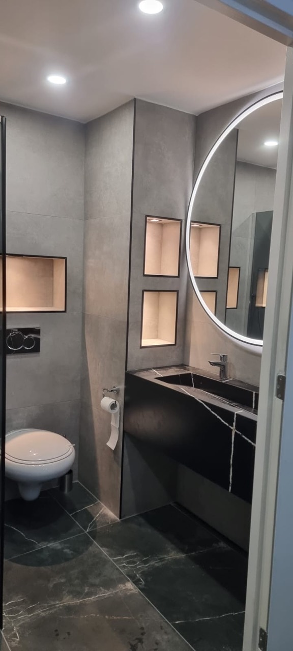 Badkamer met ronde spiegel, verlichte nissen en een donker wastafelmeubel